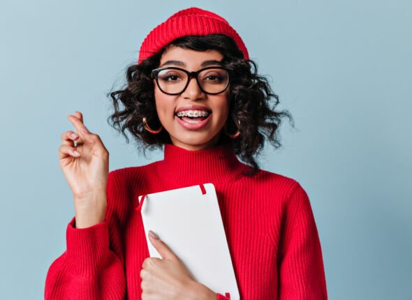 Gorgeous student with dental braces holding notebook. Mixed race girl posing with crossed fingers